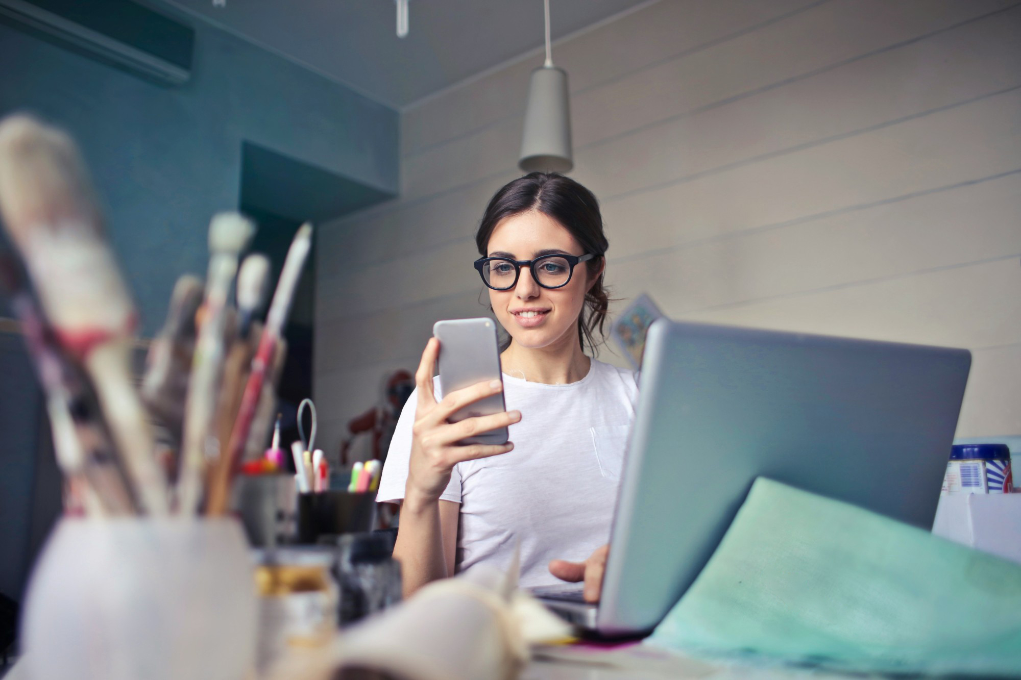 Creative professional checking finances on her phone with Rounded while working at her laptop.